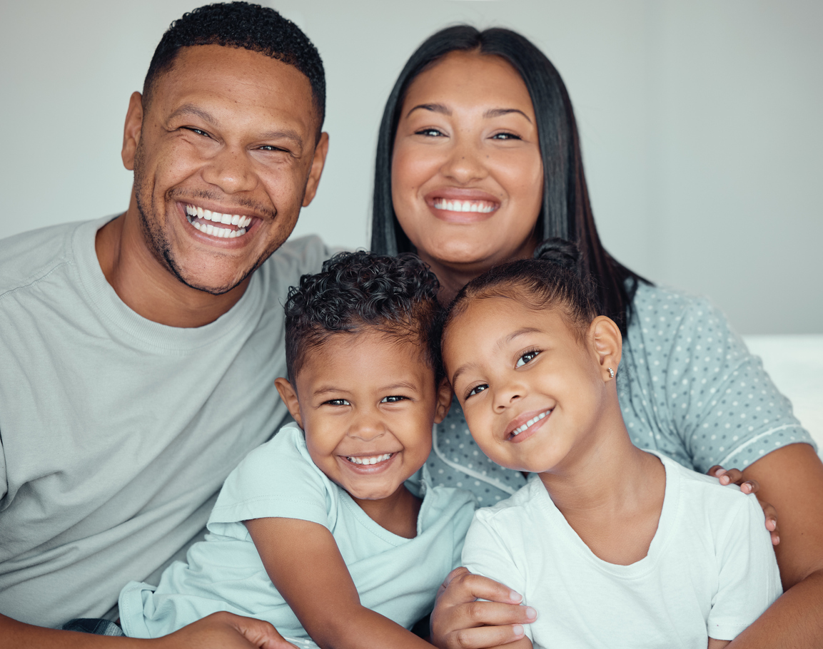 Portrait Of A Happy Young Mixed Race Family With Two Children Wearing Pyjamas And Sitting At Home Together