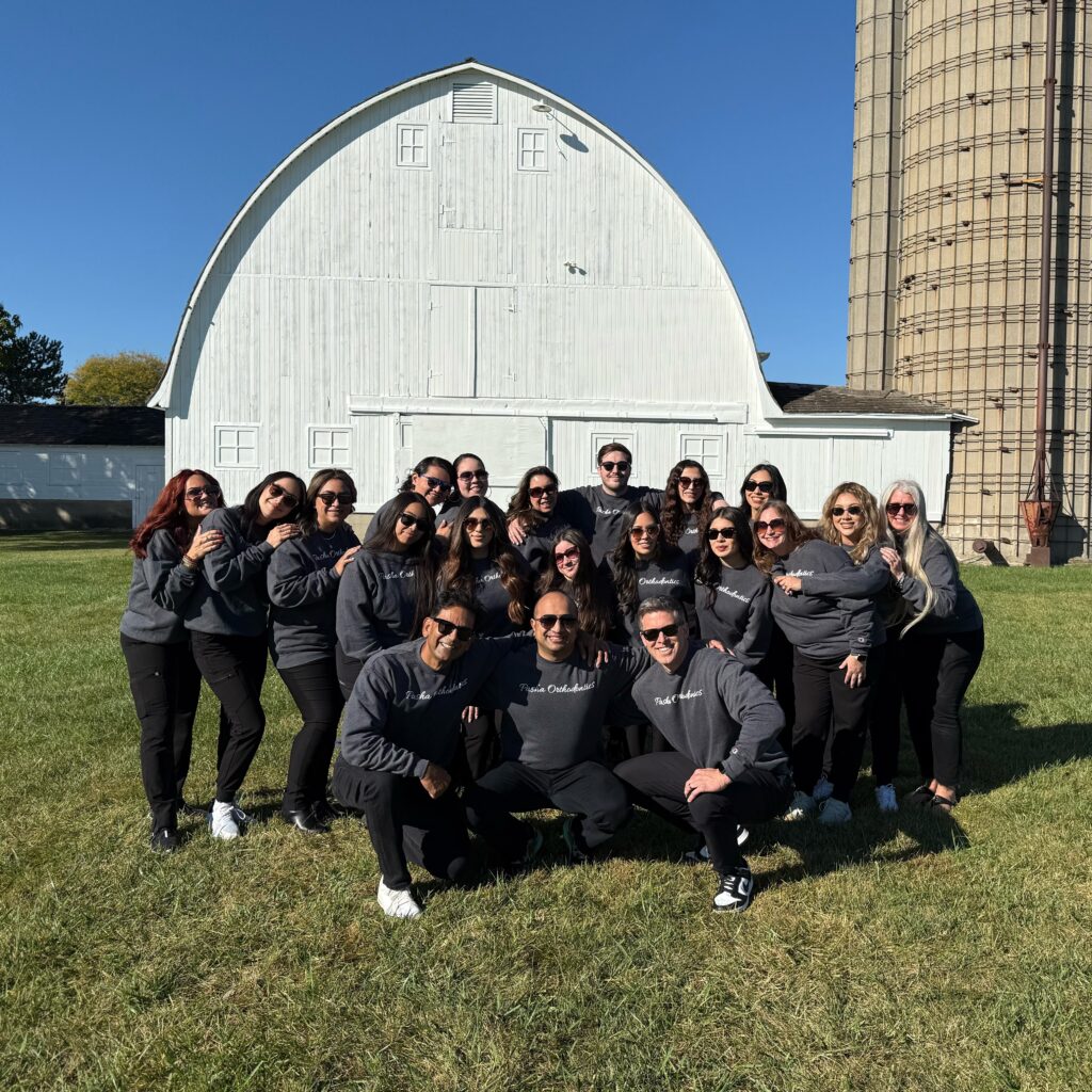 The Pasha Orthodontics Team Posing In Front Of A White Barn